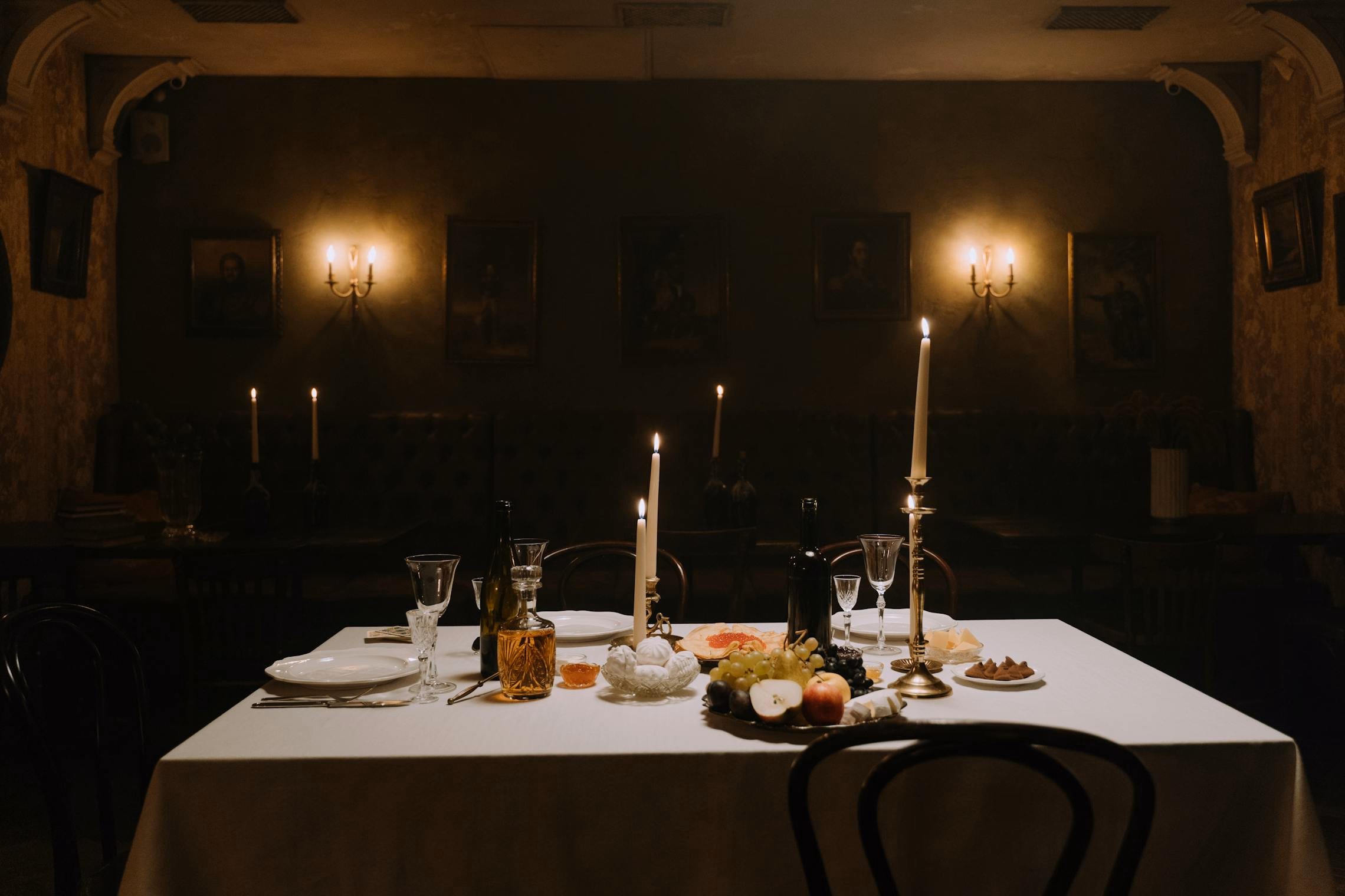 Candlelit Halloween dinner table set with black linens, gold flatware, and dark floral centerpieces