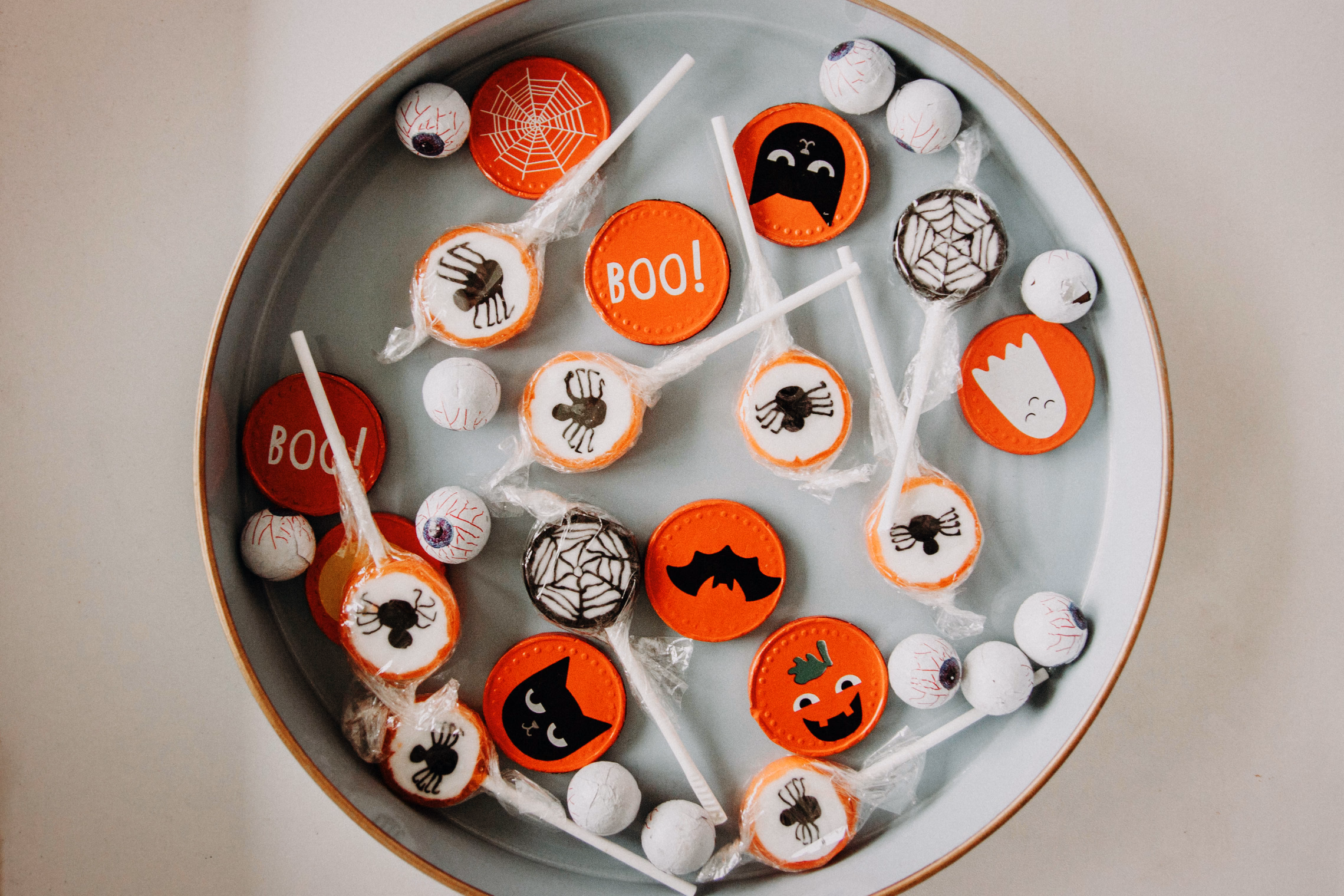A round tray of wrapped Halloween lollipops printed with spiders, bats, cobwebs and BOO, mixed with eyeball gumballs