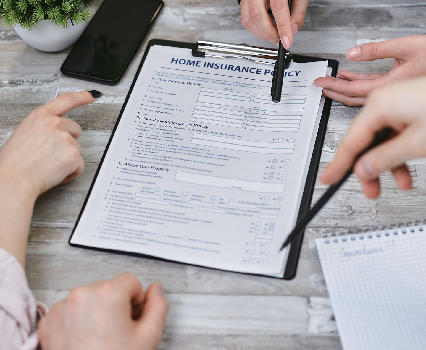 Three people at a table reviewing a home insurance policy document on a clipboard, one pointing at a line