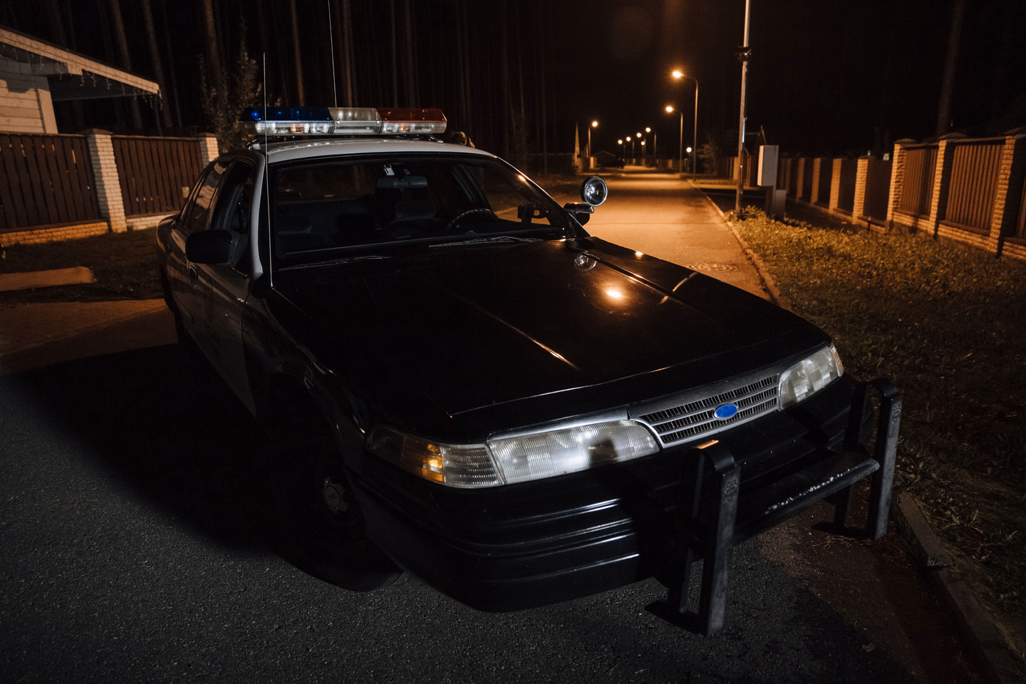A police car parked on a quiet residential street at night under streetlights