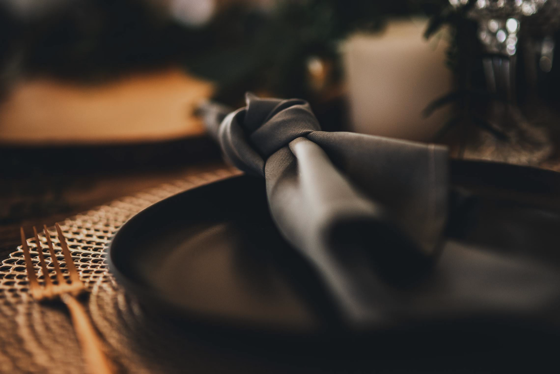 A gothic place setting with black charger plate, dark linen napkin, vintage-style flatware, and a crystal wine glass