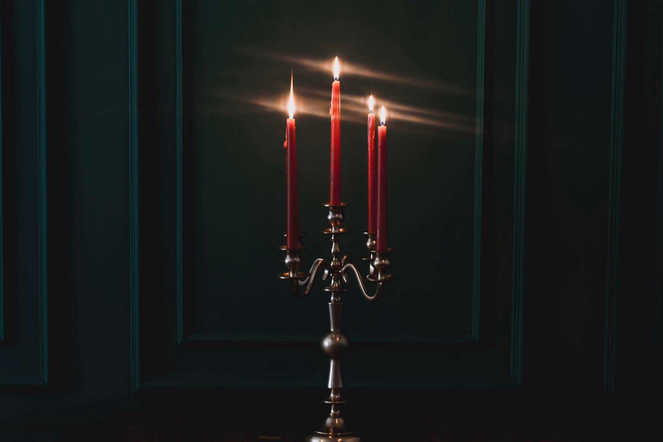 An arrangement of black and burgundy candles at varying heights with melted wax dripping down a wrought iron candelabra