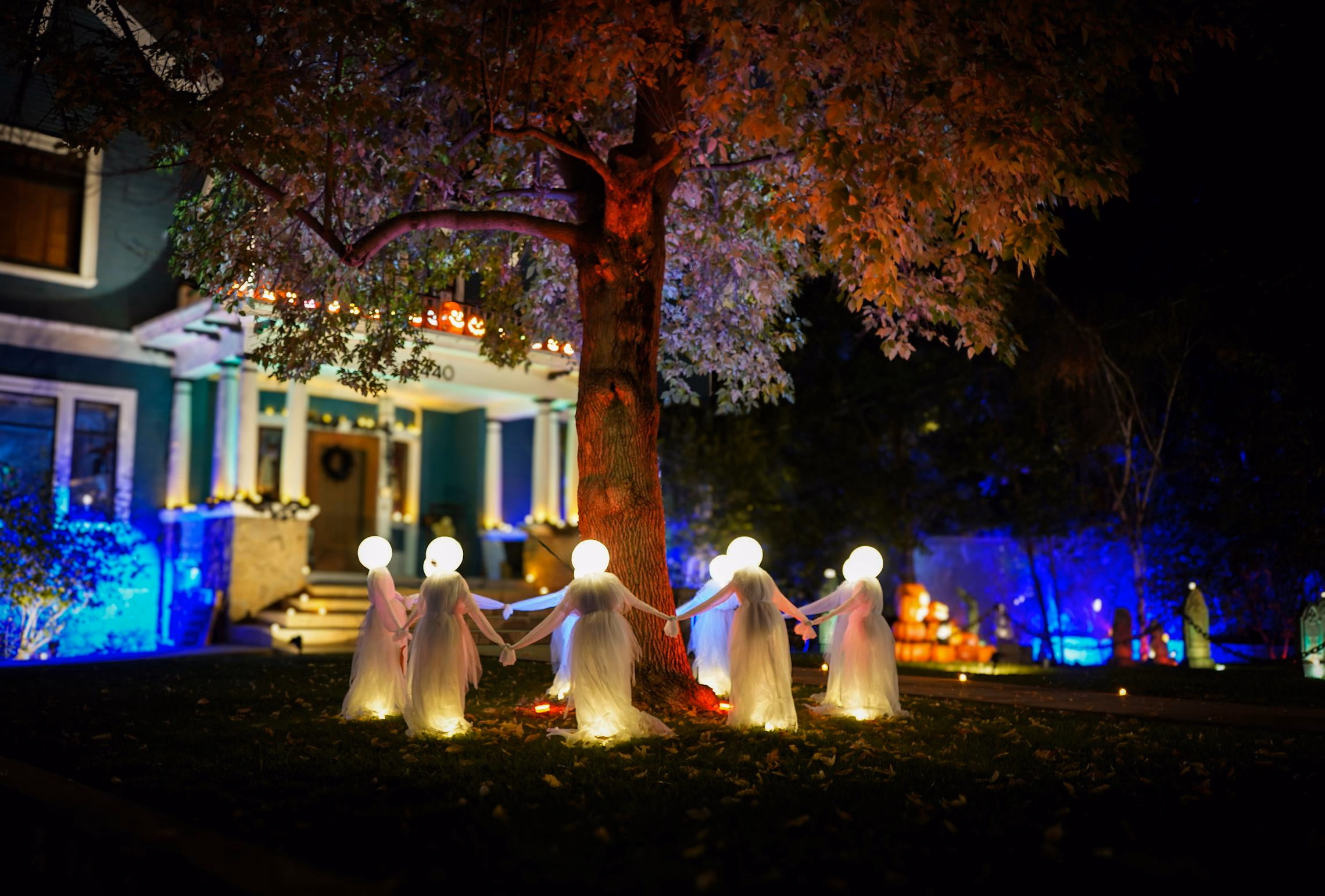 Halloween-decorated front yard with pathway lights, hanging ghosts, and ground fog